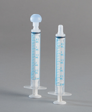 Two plastic oral syringes, one with a bulb and the other with a simple tip, sit on a gray background. The syringes are graduated in milliliters (ml) from 0.5 ml to 3 ml.