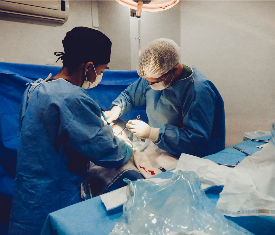 Two surgeons, wearing scrubs and masks, perform surgery on a patient in an operating room.