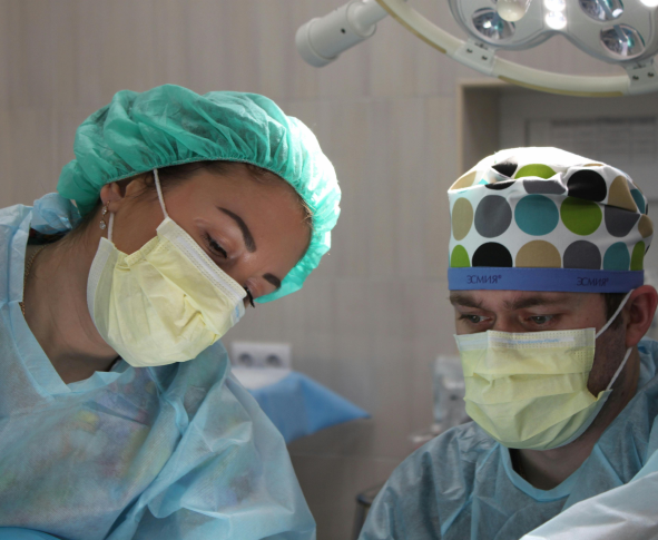 Two surgeons, wearing surgical masks and caps, are attentively observing something during a medical procedure in an operating room.
