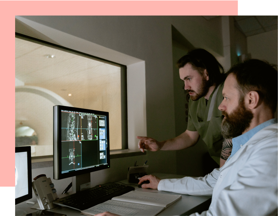 Two doctors review medical scans displayed on a computer monitor in a dimly lit office.