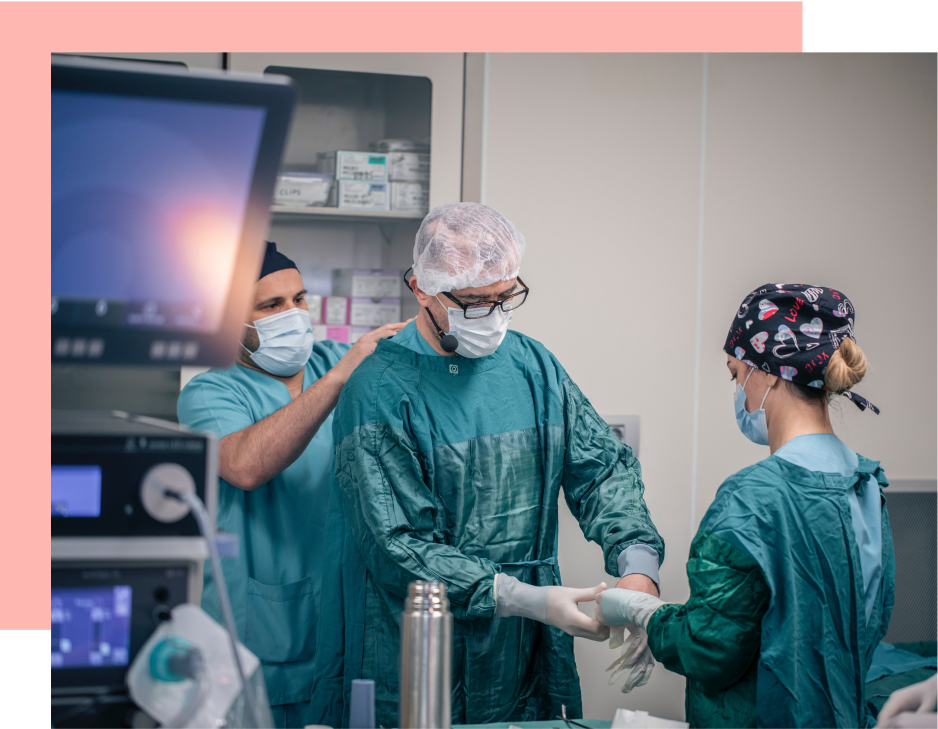 A surgeon gets dressed, assisted by two colleagues, in a sterile operating room.