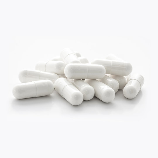 White capsules are piled loosely on a white surface.