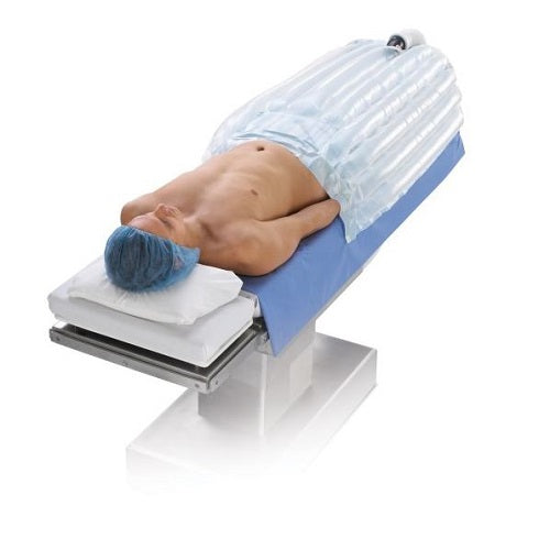 A patient lies on a surgical table, covered by an inflatable positioning device. The patient's head rests on a pillow. The context is a medical setting.