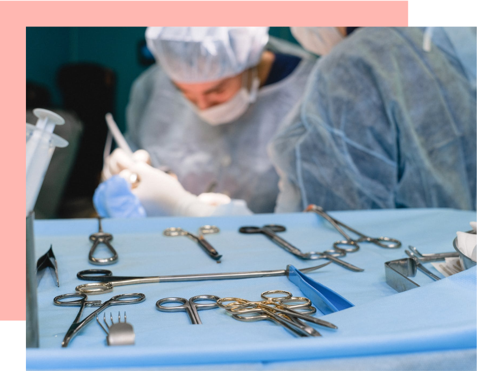 Surgical instruments lay on a blue tray; surgeons perform a procedure in the background.
