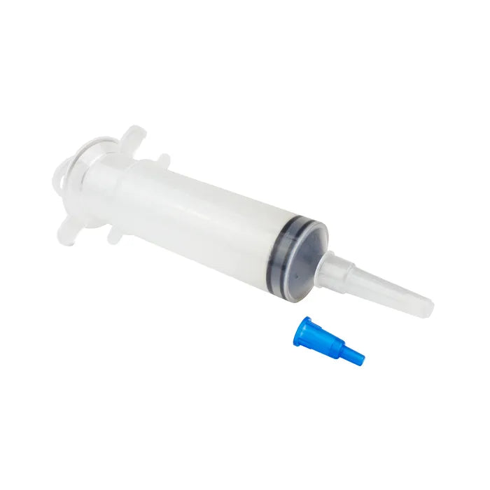 A clear plastic syringe lies disassembled on a white background; a small blue nozzle sits beside it.