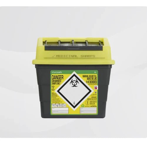 A yellow-topped, dark gray sharps container sits on a white surface. It is labeled "MEDICINAL SHARPS," "DANGER," and contains biohazard symbols. The container is for the disposal of contaminated sharps.