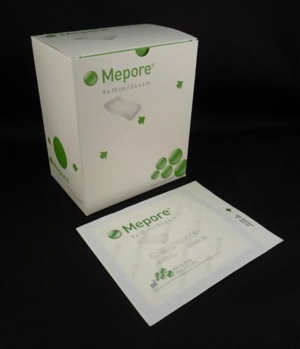 A box of gauze pads sits beside a single pad; both are white with green leaf designs and appear to be sterile.