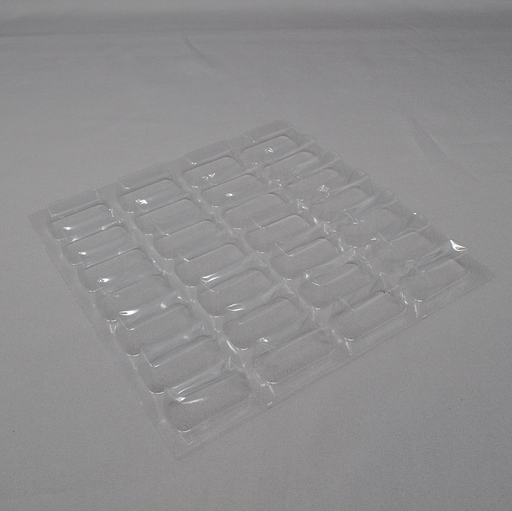 A clear plastic tray with numerous small, rectangular depressions lies on a light gray surface.