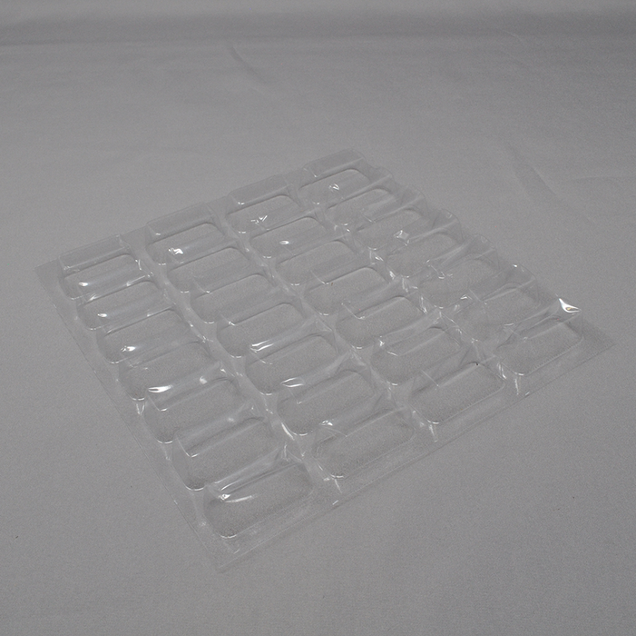 A clear plastic tray with numerous small, rectangular depressions lies on a light gray surface.