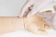 A gloved hand injects a needle into a training arm. The injection is performed on a pale, lifelike artificial arm, likely for medical training purposes.