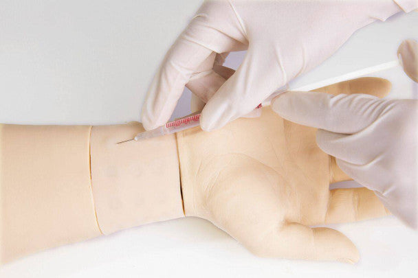 A gloved hand injects a needle into a training arm. The injection is performed on a pale, lifelike artificial arm, likely for medical training purposes.