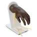 A dark brown prosthetic hand rests on a white stand, its fingers slightly splayed. Yellow cords, seemingly veins, extend from the wrist and drape down the stand.