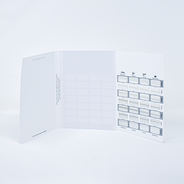 A medication organizer displays a weekly pill schedule; it is opened to reveal daily and time-specific compartments, situated on a plain white surface. ARTICLASSICS is printed on the side.