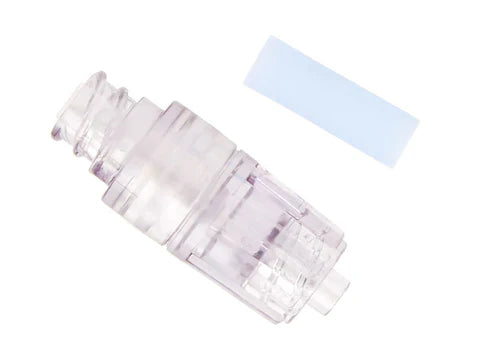 A transparent medical connector rests beside a light blue, rectangular filter on a white background.