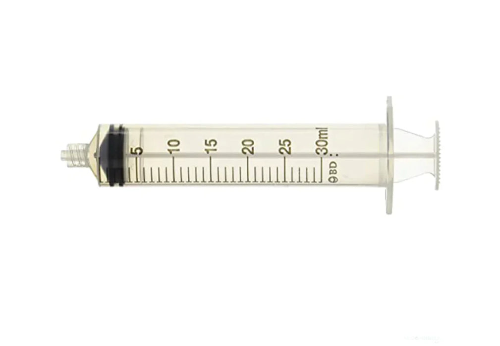 A clear plastic syringe, rests on a white background. It is marked with milliliter graduations from 5 to 30 ml, and bears the BD logo.