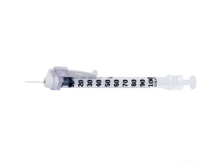 A syringe lies horizontally on a plain white background. The syringe is transparent with black markings along its barrel.