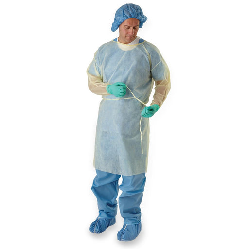 A pale-yellow disposable gown is being tied by a person wearing teal gloves and a blue surgical cap against a white background.
