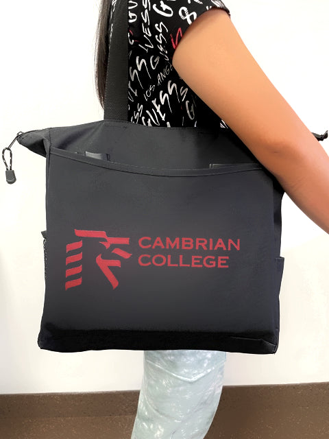 A black tote bag, featuring the logo “CAMBRIAN COLLEGE,” is being carried by a person.