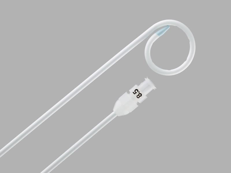 A long, thin, white catheter, curved at one end, lies alongside a smaller, connector piece marked "8.5," against a gray background.