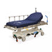 A stretcher rests on wheels, featuring a dark blue mattress; it's in a sterile environment. The text on the mattress reads "AirMax." The stretcher is labeled "Hill-Rom."