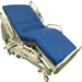 A hospital bed rests on wheels, featuring a blue mattress. The bed is in an elevated position.