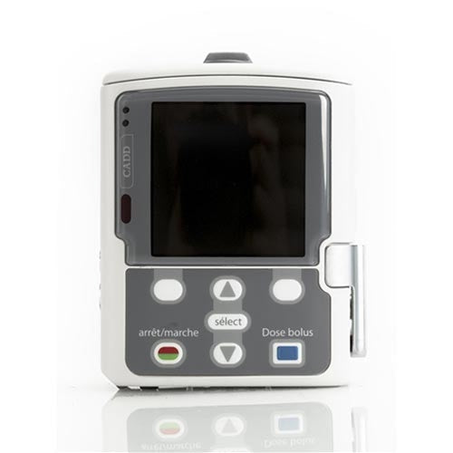 A CADD ambulatory infusion pump displays its screen; buttons labeled “arrêt/marche,” “sélect,” and “Dose bolus” are visible. It sits on a reflective white surface.