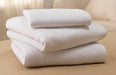 A neatly folded stack of white sheets sits on a light beige surface. The sheets appear soft and are likely made of cotton or a similar material.