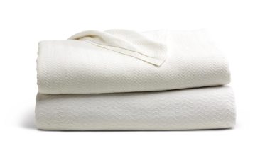 Two off-white blankets are stacked neatly on a plain white background. A small portion of a tag or label is visible on top.