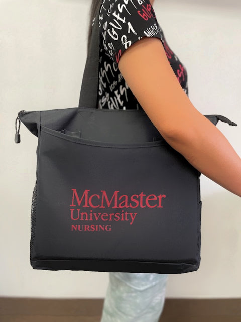 A black McMaster University Nursing tote bag is being carried by a person. McMaster University NURSING is printed on the bag.