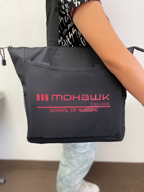 A black tote bag, featuring the Mohawk College School of Nursing logo, is being carried by a person.