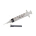A clear plastic syringe rests on a white background; a separate black needle lies beside it.