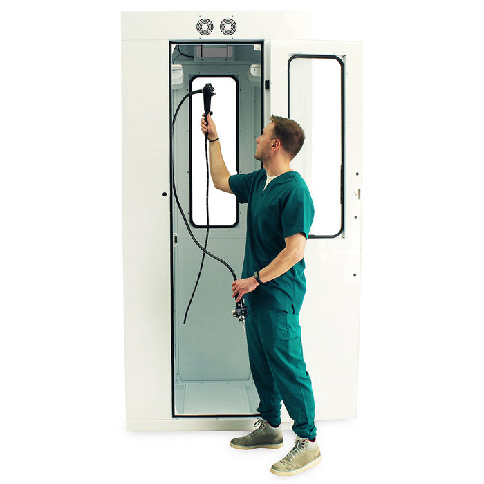 A medical professional operates an endoscopy device inside a white, enclosed medical booth.