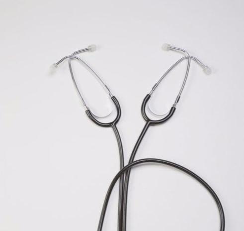 Two stethoscopes lie on a white surface, their earpieces pointing outwards. They are arranged in a loose X shape.