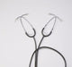 Two stethoscopes lie on a white surface, their earpieces pointing outwards. They are arranged in a loose X shape.