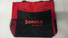 A red and black tote bag sits upright. The bag displays the logo "Seneca Nursing" in a stylized font. Side mesh pockets are visible.