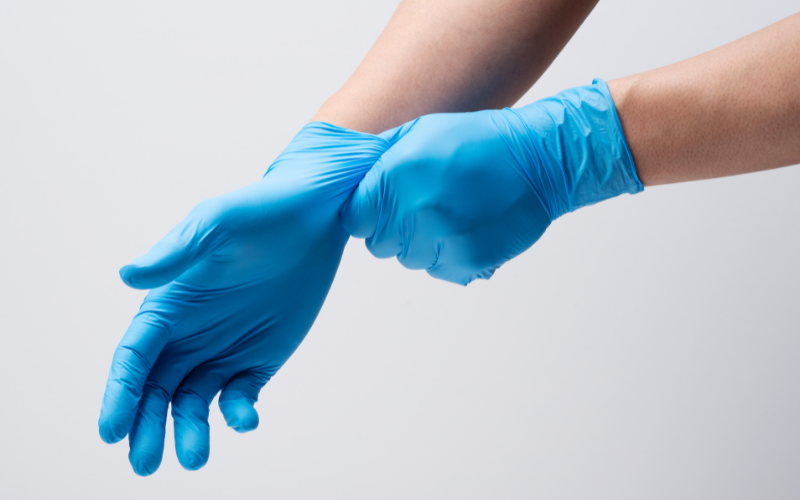 Two hands put on blue nitrile gloves against a white background.