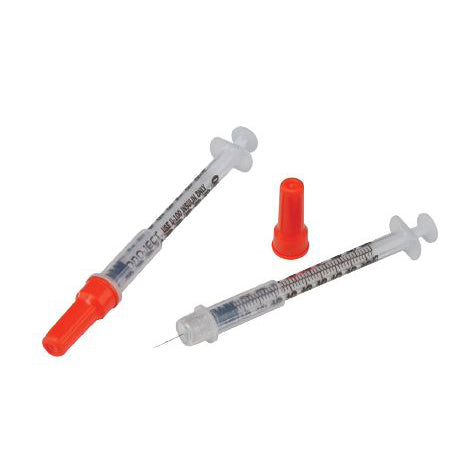 Two syringes lie on a plain white background; one is capped with a red plastic tip. A separate red cap is also present.