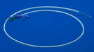 A translucent, thin catheter lies coiled on a solid blue background. A small, multicolored connector is visible at one end.