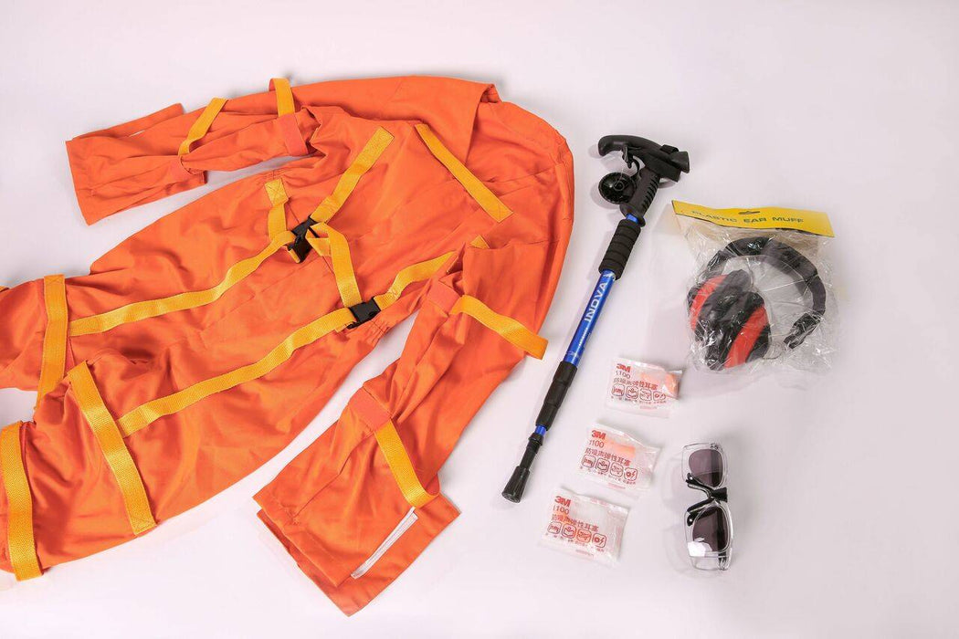 An orange jumpsuit lies on a white surface, accompanied by a walking stick, earmuffs, earplugs, and safety glasses.