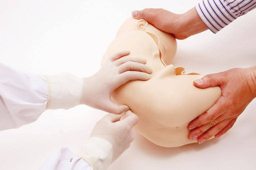A medical mannequin is being manipulated by gloved hands on a white surface. Multiple people are involved in the process.
