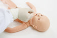 A gloved hand inserts a tube into a baby mannequin's nose. The mannequin lies supine on a white surface.