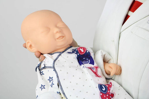 A lifelike baby doll is being held gently by a person wearing a white lab coat, in what appears to be a clinical setting.