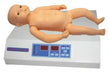 A plastic baby doll lies flat on its back on a white digital scale. The scale has a dark-colored display and button controls on the front.