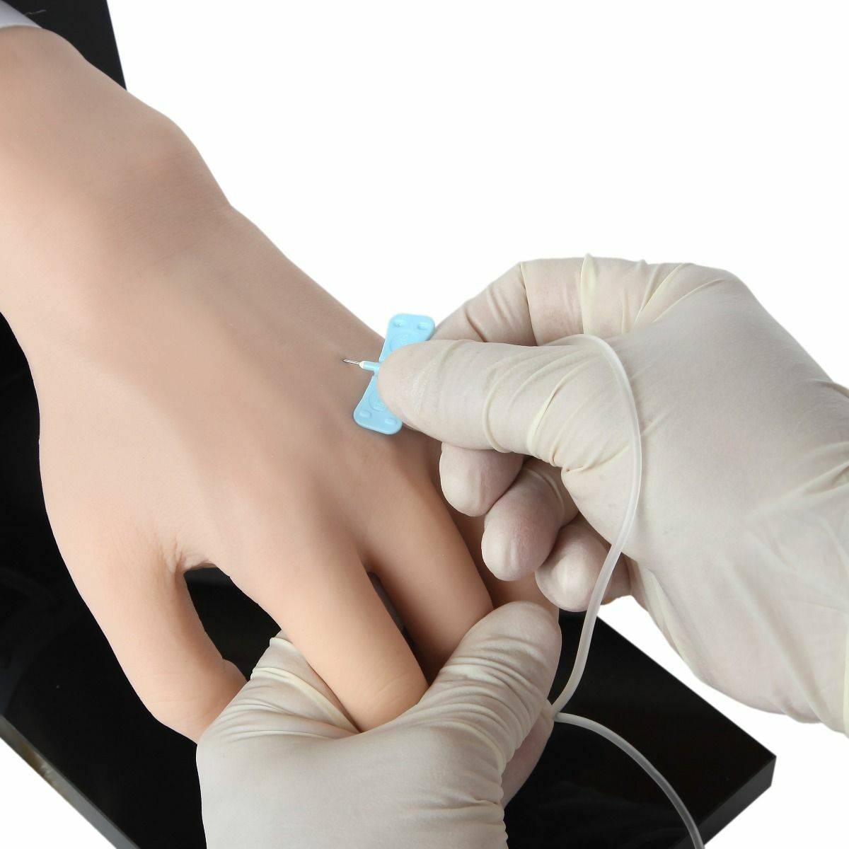 A gloved hand inserts a cannula into a realistic training hand; the setup rests on a black surface.