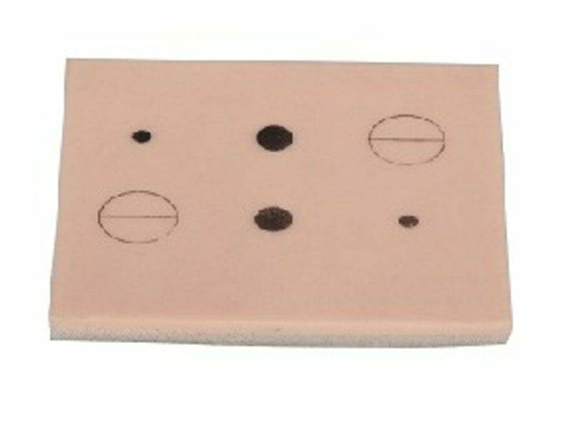 A light-brown, rectangular simulated skin pad features varying sizes and shapes of dark lesions and imperfections. The pad is set against a plain white backdrop.