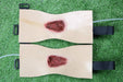 Two tan fabric pads, each with a simulated wound, are fastened with black straps. They lie on a green surface.