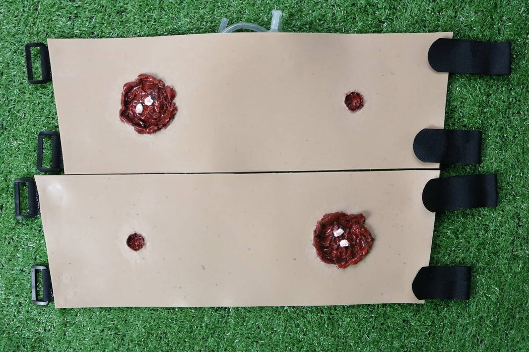 Two tan, simulated-skin panels, each showing simulated wounds, are fastened with black straps; they lie on artificial turf.