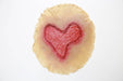 A flesh-colored, irregular disc displays a red heart-shaped mark. The mark appears to be a wound or imprint. The disc rests on a white background.