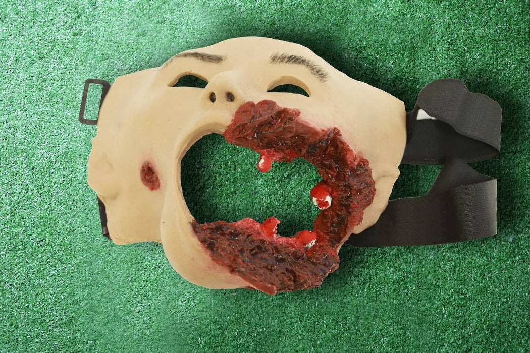 A grotesque face mask, depicting a severely injured face, rests on artificial turf.