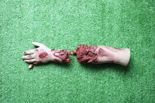 A severed, bloody arm lies on artificial turf; the hand is outstretched.